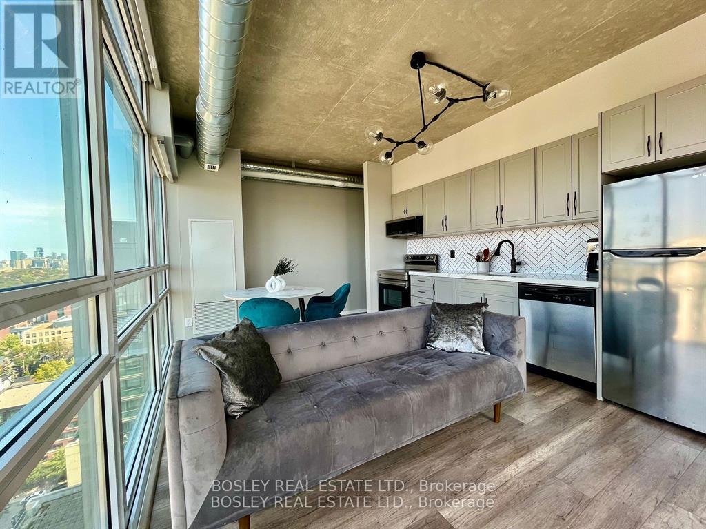 A modern kitchen and living room with a grey couch and stainless steel appliances.