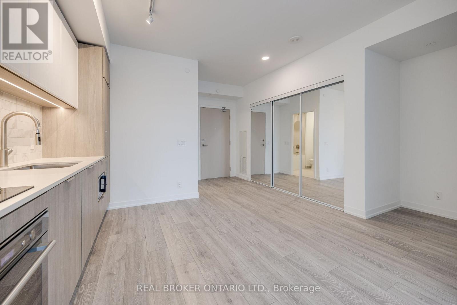 A spacious, empty room with a kitchen area to the left and a sliding glass door leading to another room.