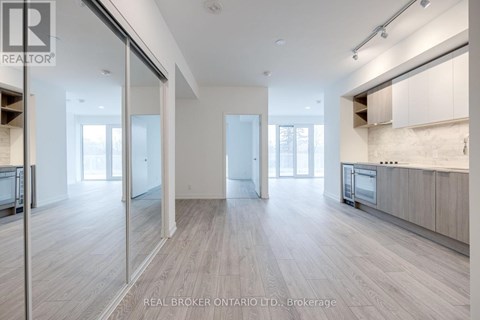 A spacious, well-lit room with wooden flooring and a kitchen area with white cabinets and appliances.