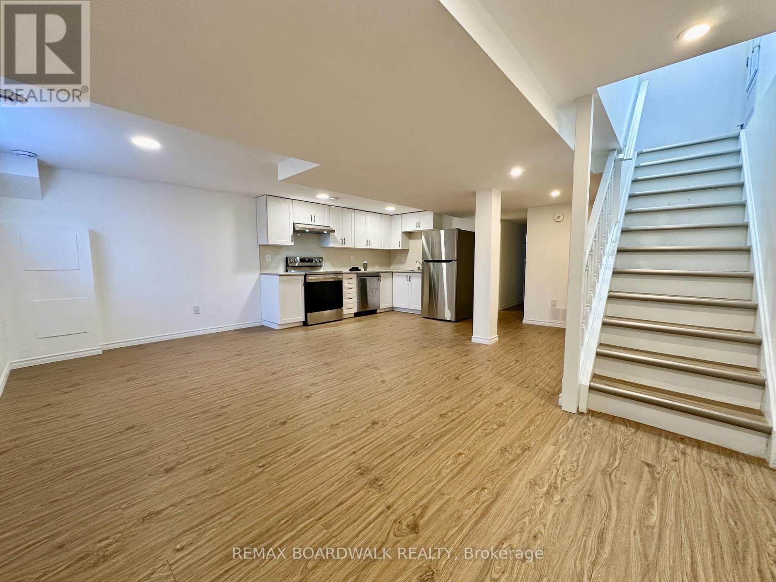 A spacious room with wooden flooring and a staircase on the right side.