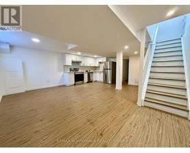 A spacious room with wooden flooring and a staircase on the right side.