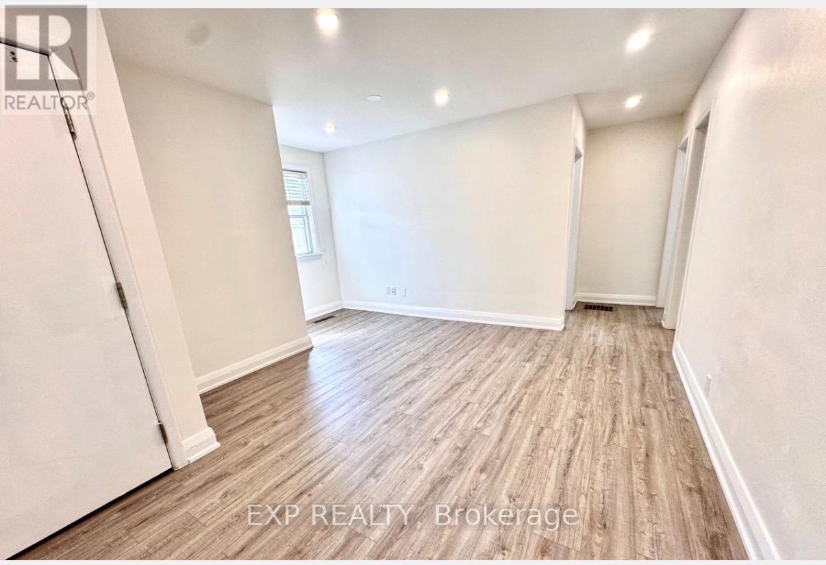 A room with wooden flooring and white walls, with a door on the left and a window on the right.