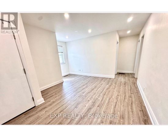 A room with wooden flooring and white walls, with a door on the left and a window on the right.
