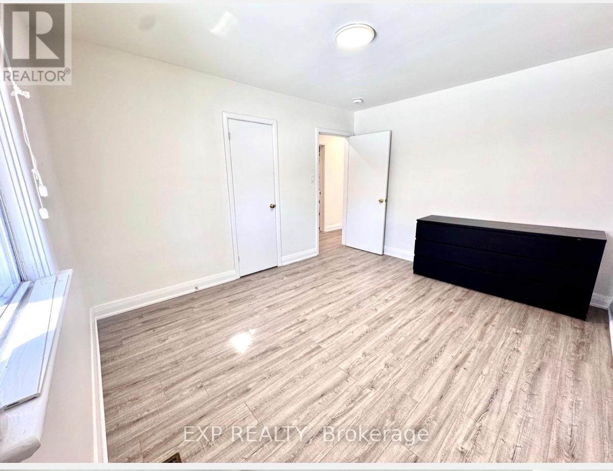 A room with wooden flooring and white walls, with a window on the left side.