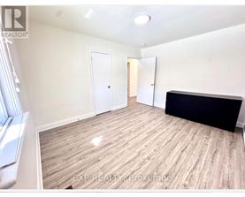 A room with wooden flooring and white walls, with a window on the left side.