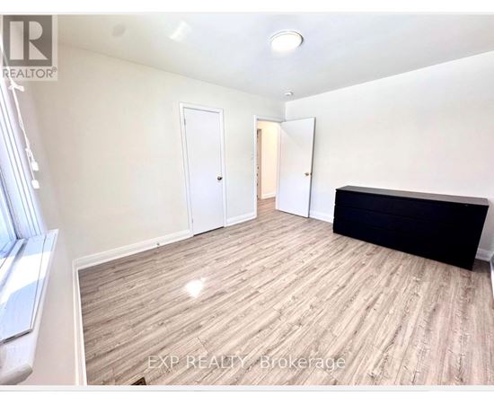A room with wooden flooring and white walls, with a window on the left side.