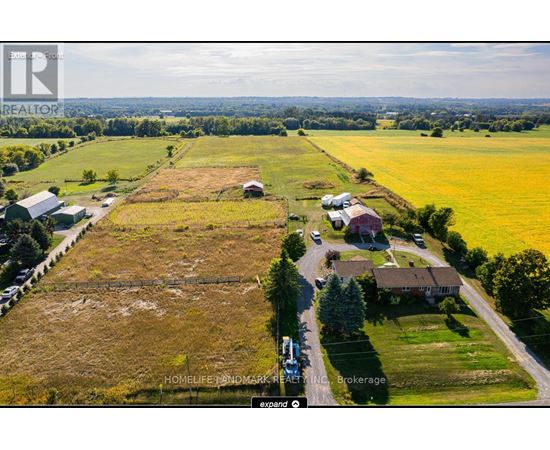 An aerial view of a rural property with a large field, a few buildings, and a road.