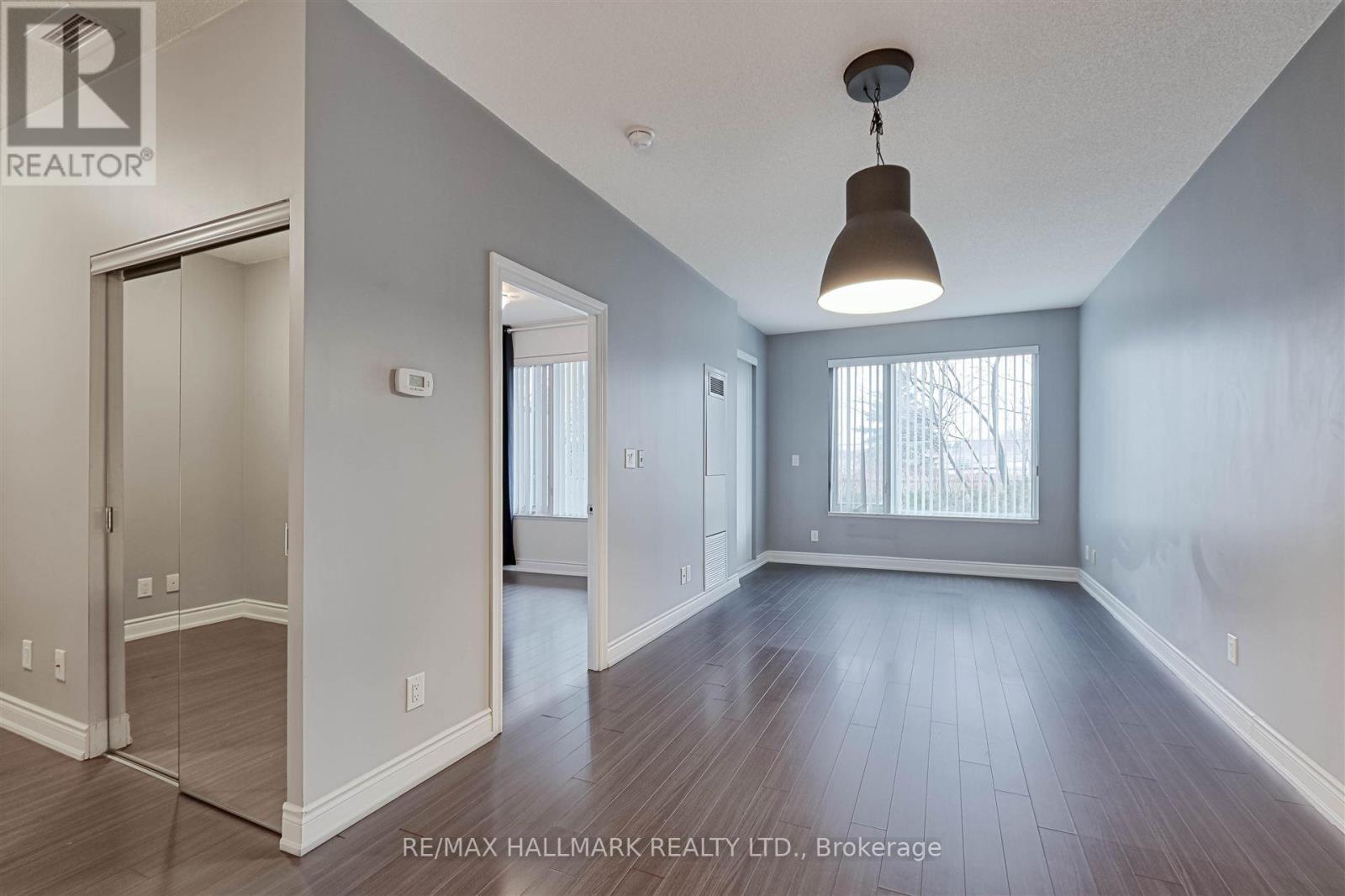 A spacious room with wood flooring and a large window with blinds.