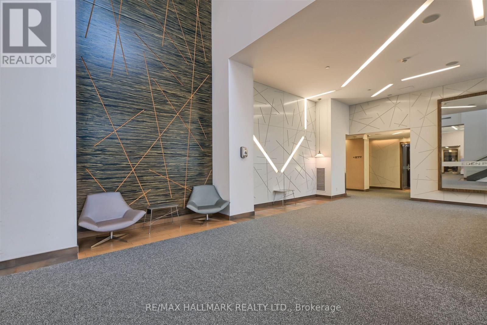 A hallway with a carpeted floor, a mirror, and a wall with a geometric pattern.