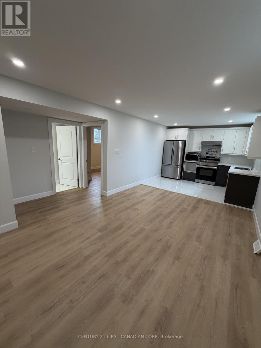 A spacious room with wooden flooring and a kitchen area in the background.