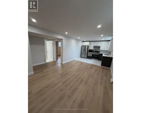 A spacious room with wooden flooring and a kitchen area in the background.