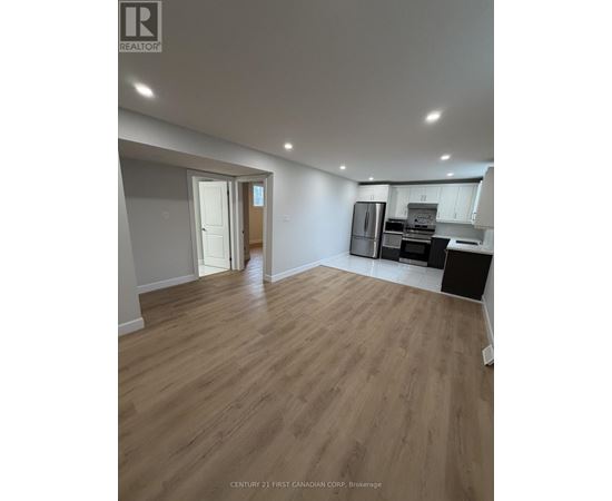 A spacious room with wooden flooring and a kitchen area in the background.