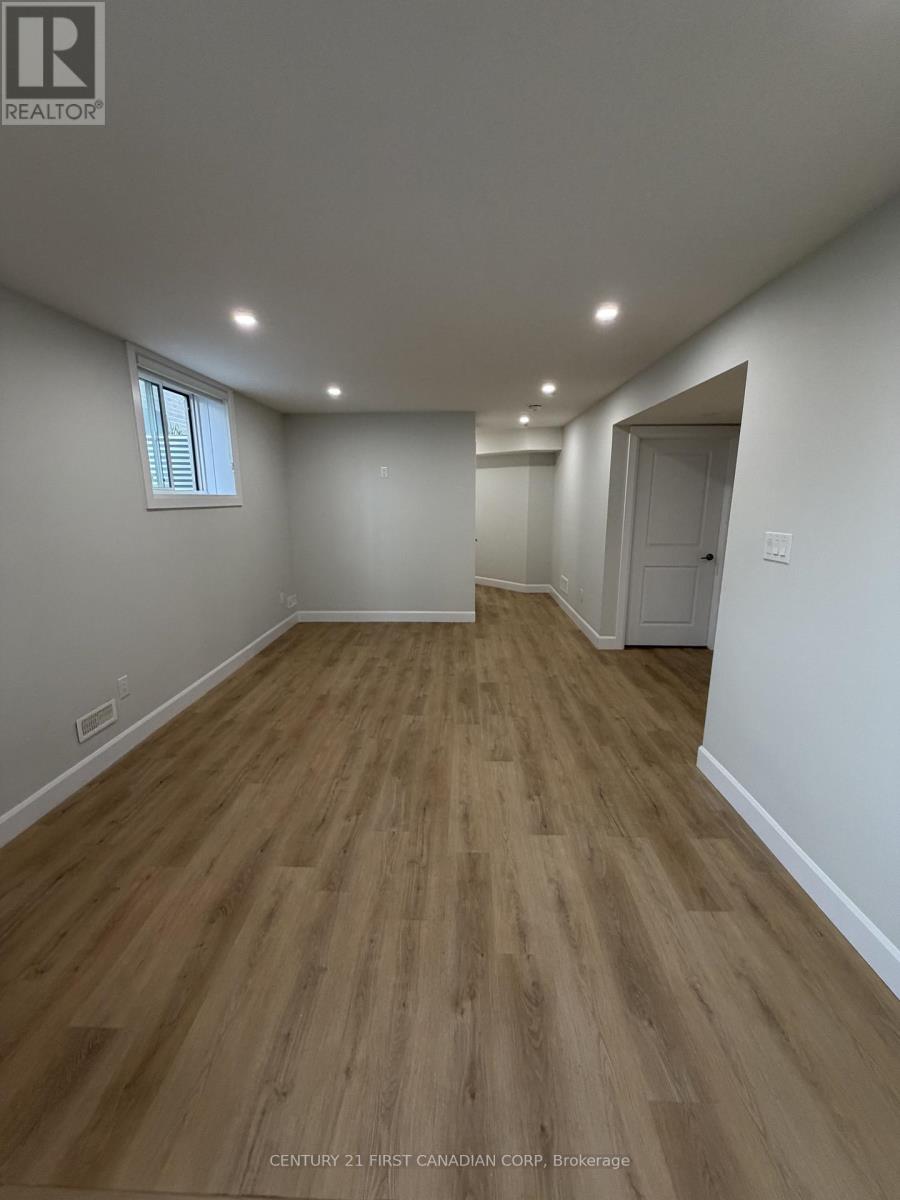 A room with wooden flooring and white walls, with a window on the left wall.