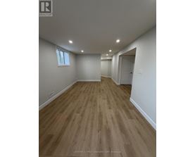A room with wooden flooring and white walls, with a window on the left wall.