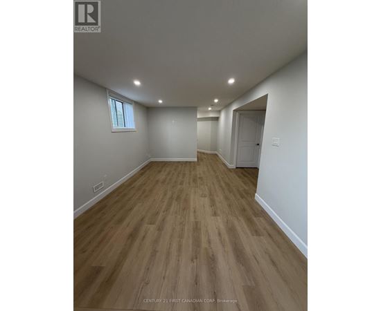 A room with wooden flooring and white walls, with a window on the left wall.