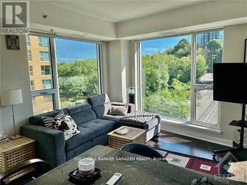 A living room with a grey couch and a large window overlooking a forest.