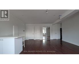 A spacious room with wooden floors and white walls, featuring a kitchen area with white cabinets.