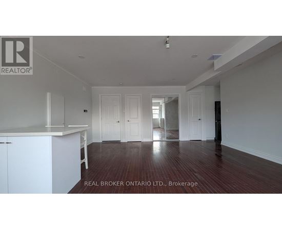 A spacious room with wooden floors and white walls, featuring a kitchen area with white cabinets.