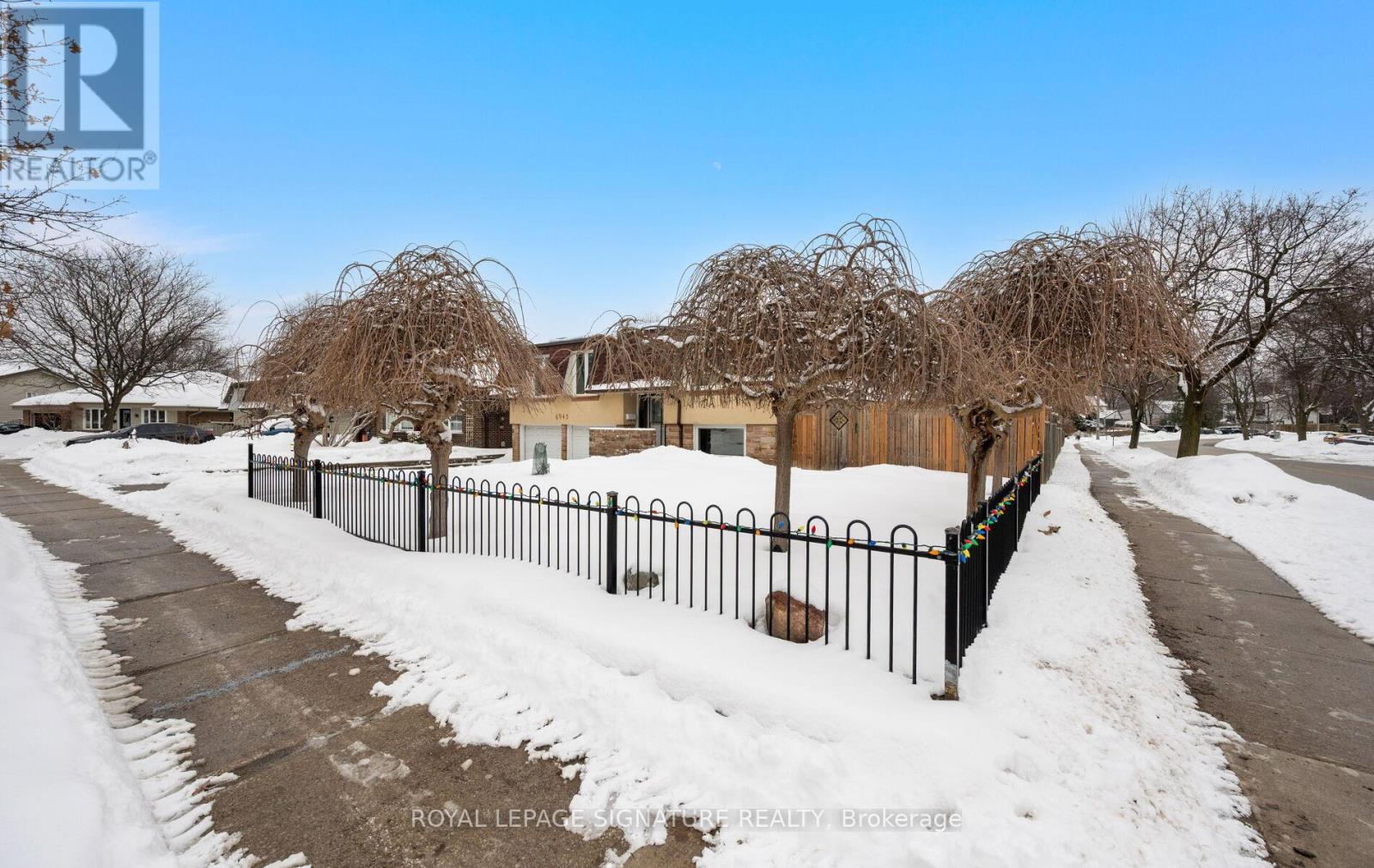 A snow-covered street with a fence and trees in the background.