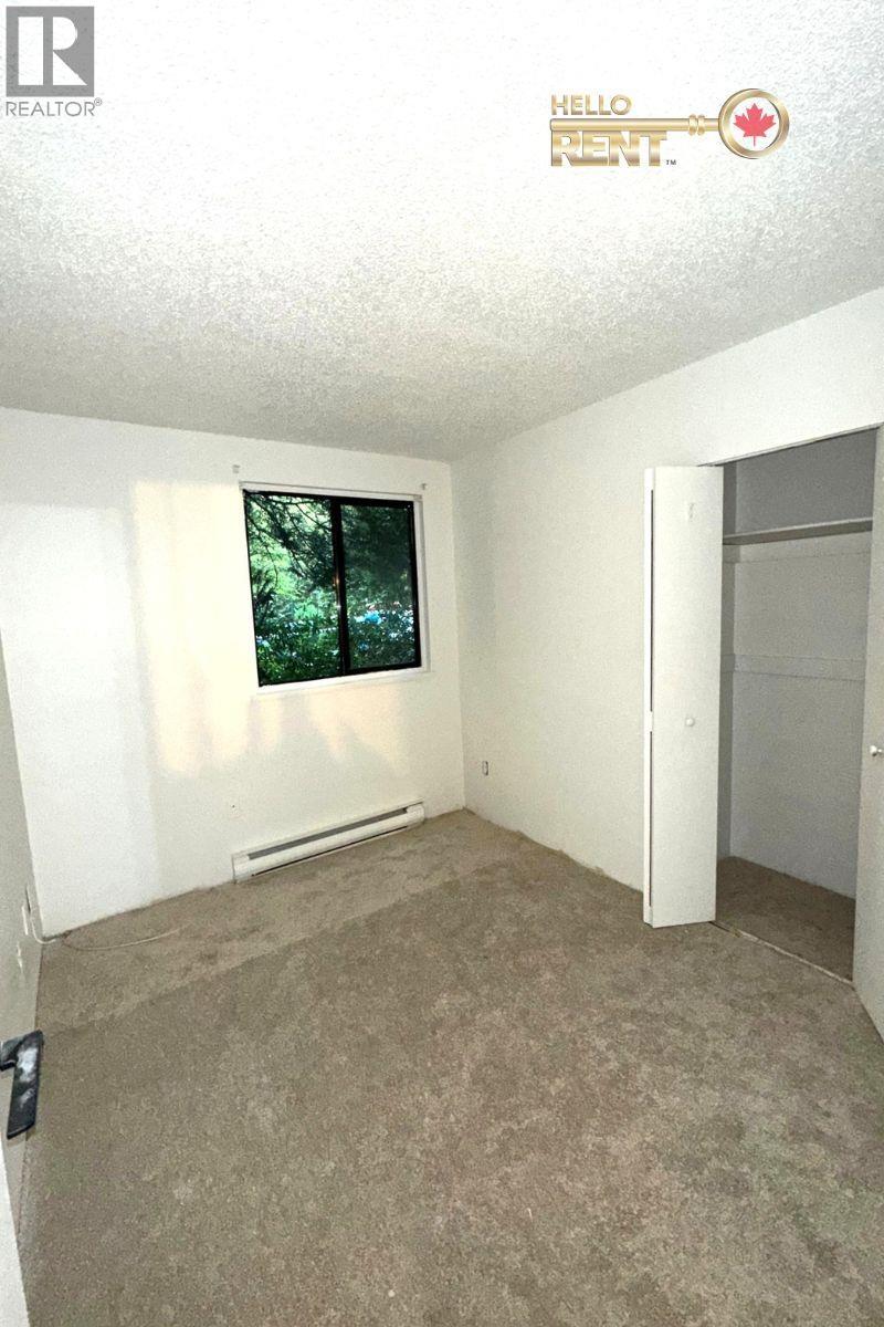 A room with a carpeted floor and a window with a view of trees.