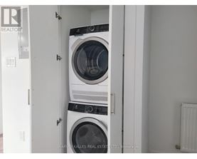 Two washing machines are stacked in a small, white laundry room.