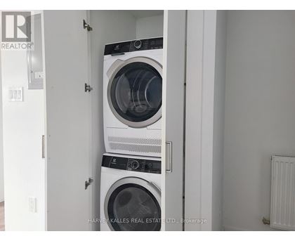 Two washing machines are stacked in a small, white laundry room.