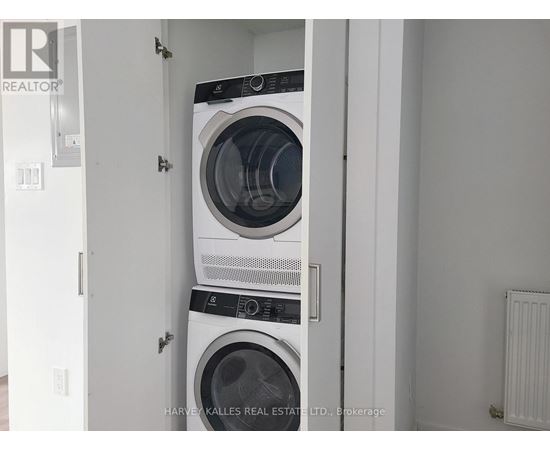 Two washing machines are stacked in a small, white laundry room.