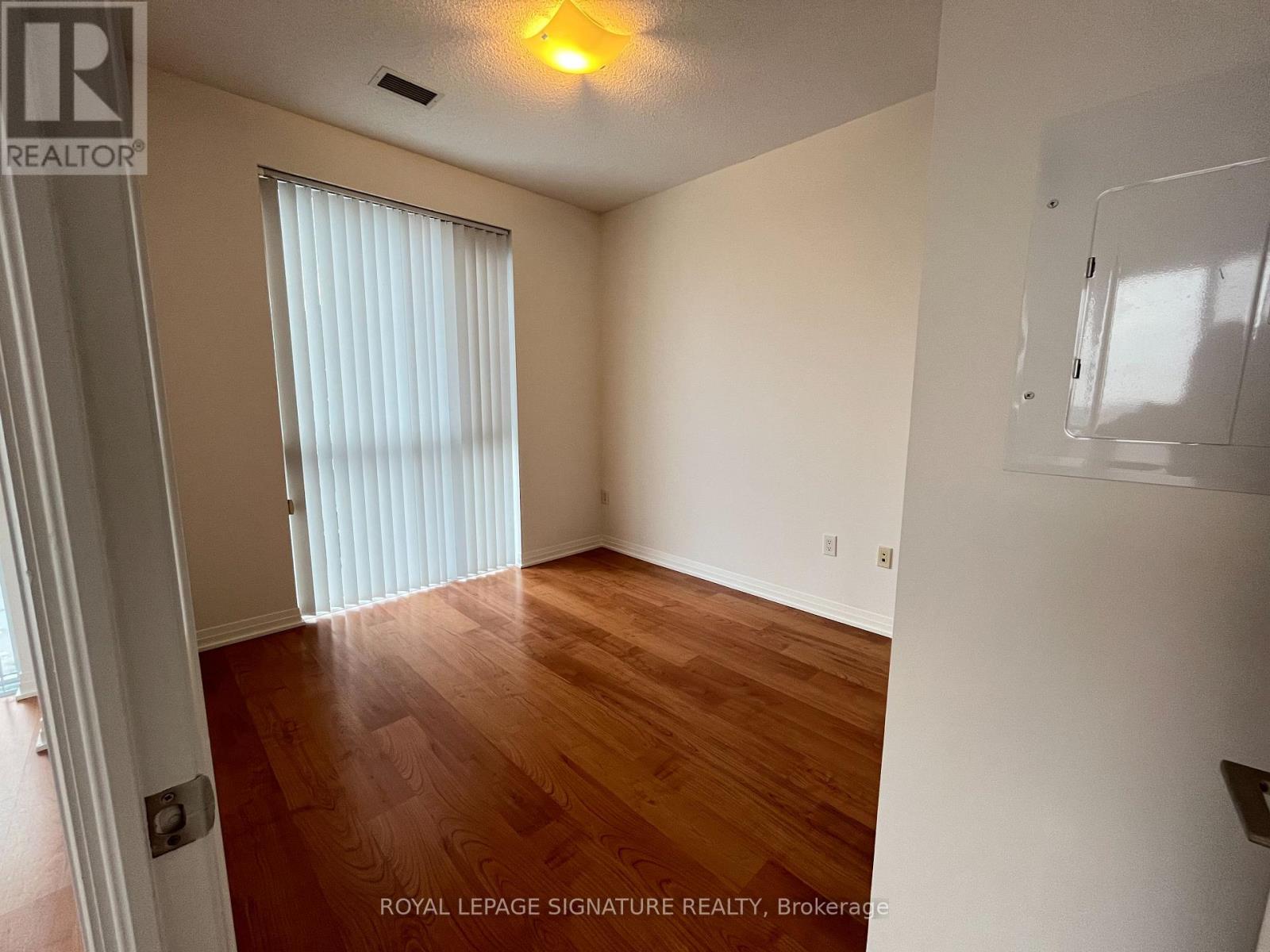 A room with wooden floors and white walls, with a window covered by white blinds.