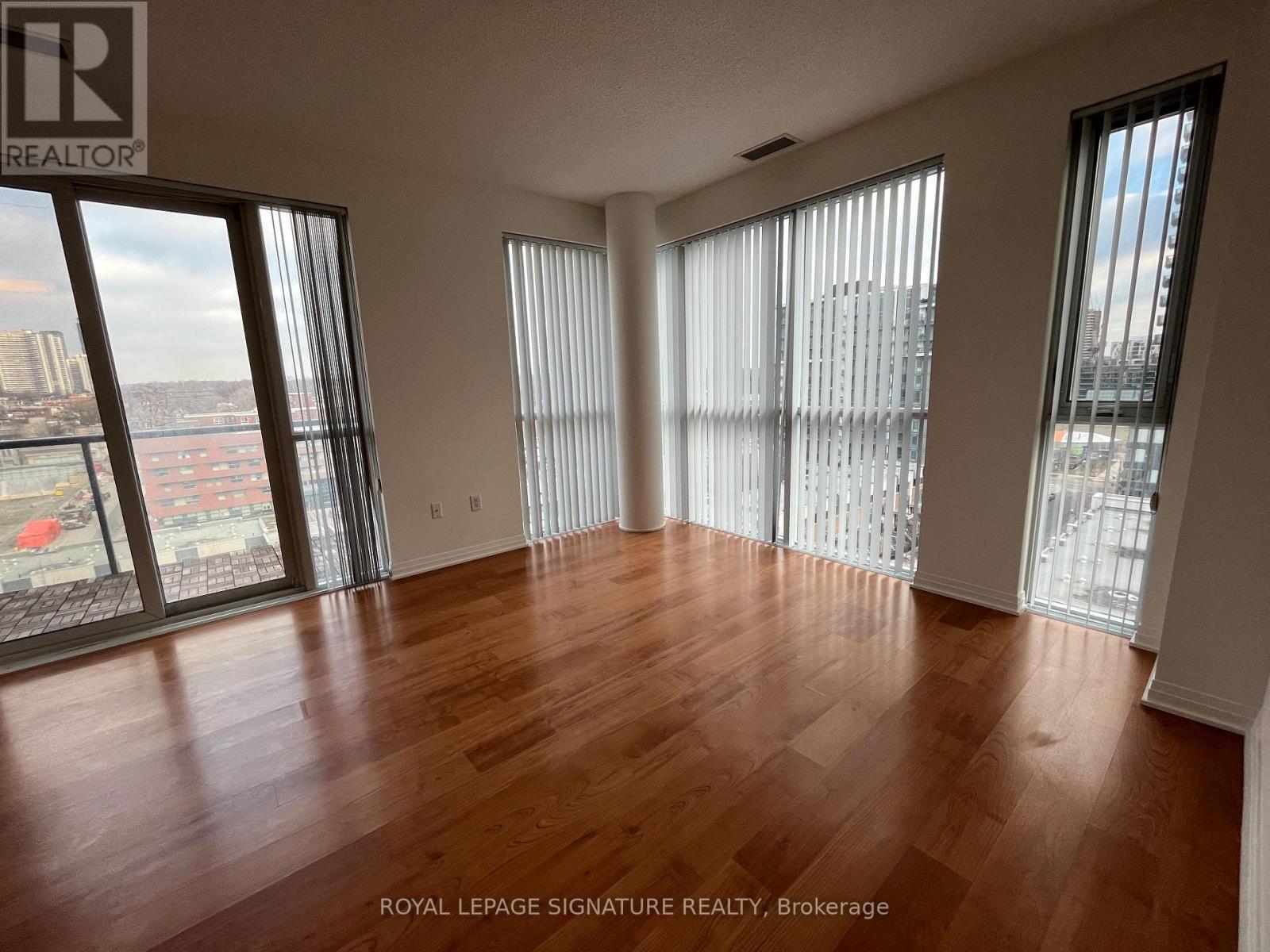 A room with wooden flooring and large windows overlooking a cityscape.
