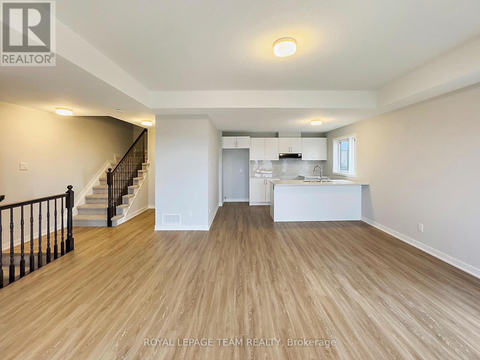 A spacious room with wooden flooring and a staircase with black railings.
