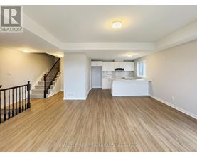 A spacious room with wooden flooring and a staircase with black railings.