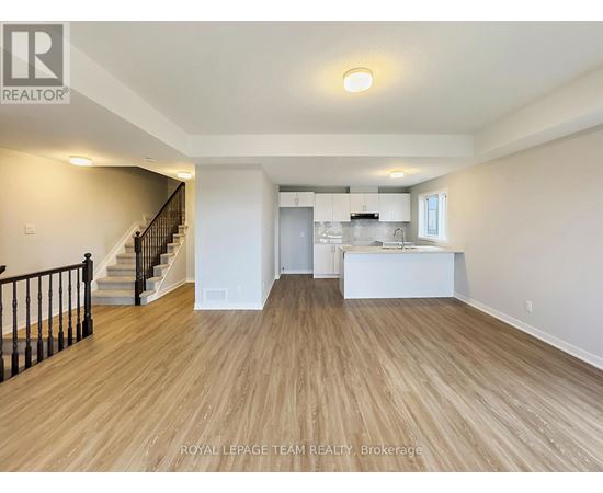 A spacious room with wooden flooring and a staircase with black railings.