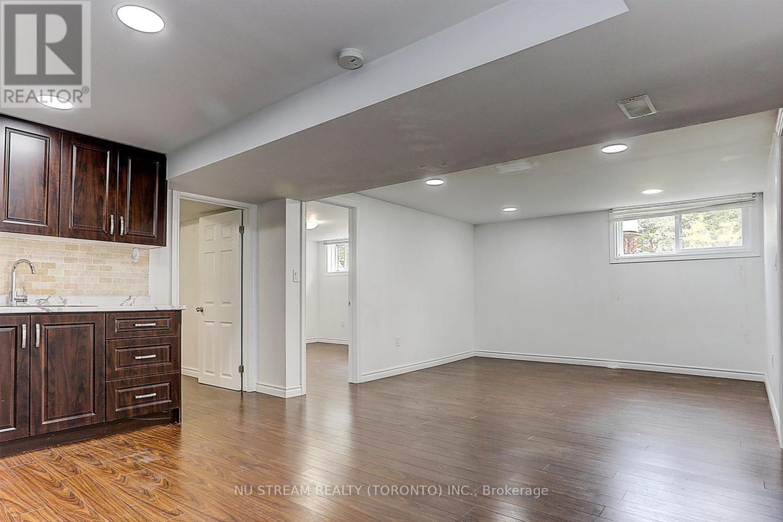 A room with wooden floors and white walls, with a kitchen area to the left.