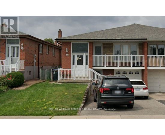 A black car is parked in front of a house with a white fence.