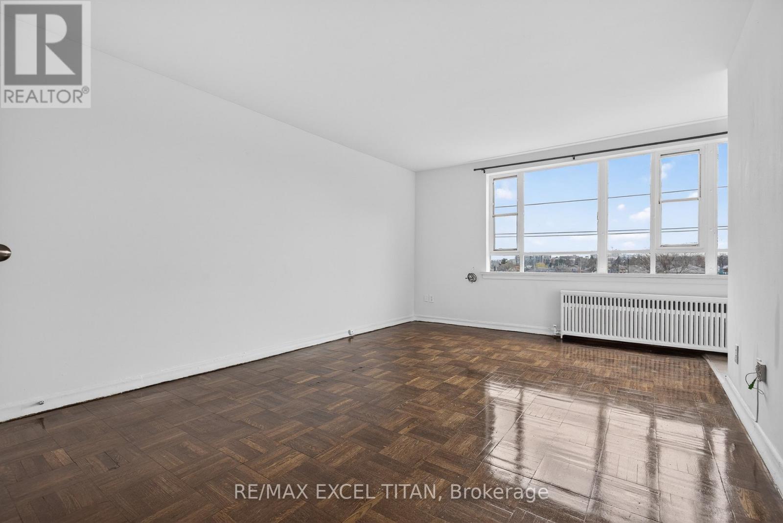A spacious room with wooden flooring and a large window overlooking a snowy landscape.