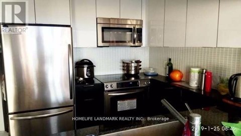 A kitchen with a stainless steel refrigerator and black countertops.