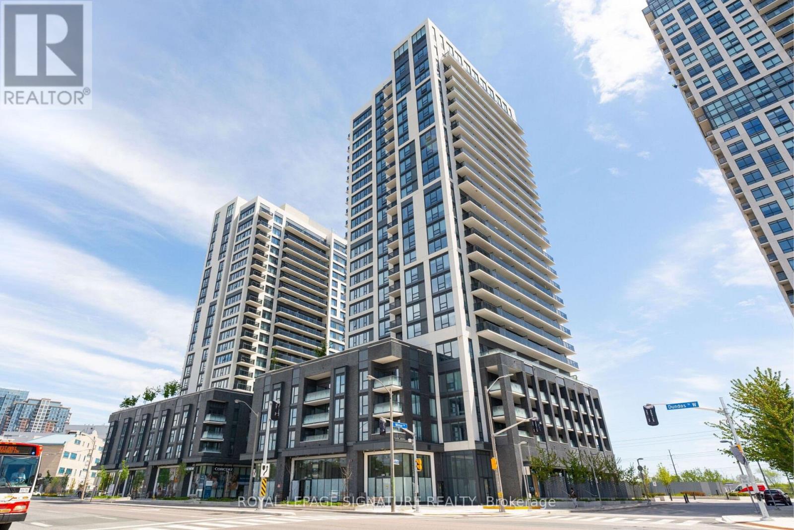 A modern multi-story building with a glass facade stands in front of two other buildings.