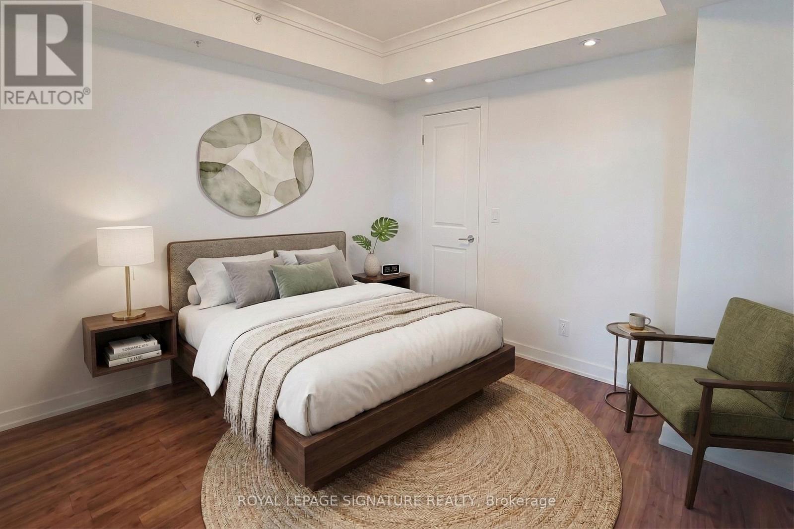 A bedroom with a large bed, a side table with a lamp, a chair, and a rug.