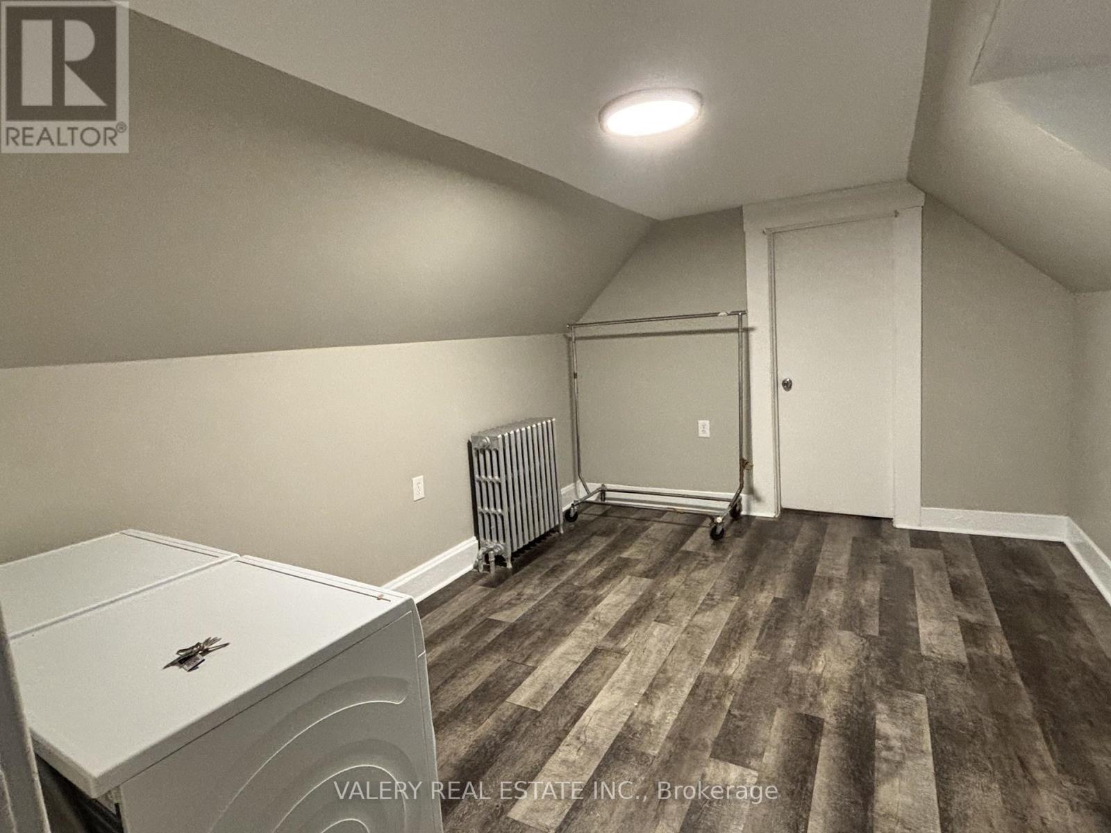 A room with a white fridge and a wood floor.