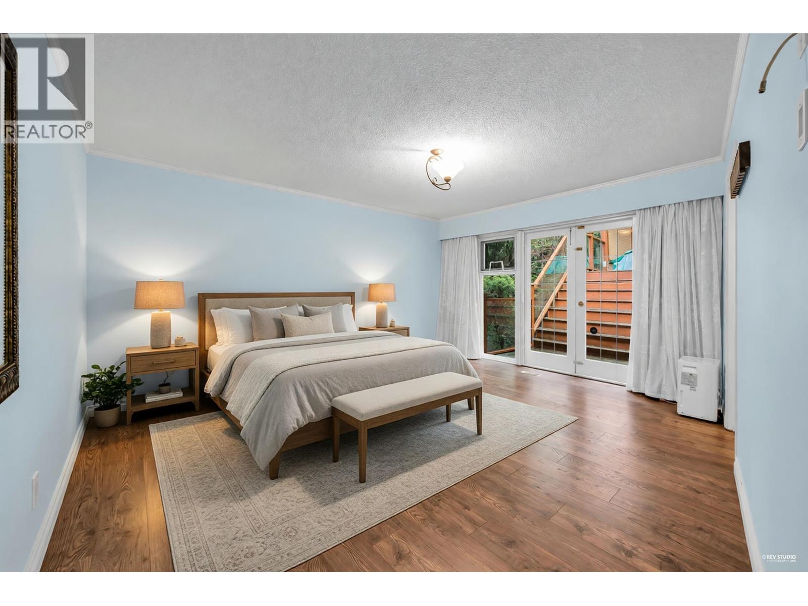 A bedroom with a bed, nightstands, and a window with a view of a deck outside.