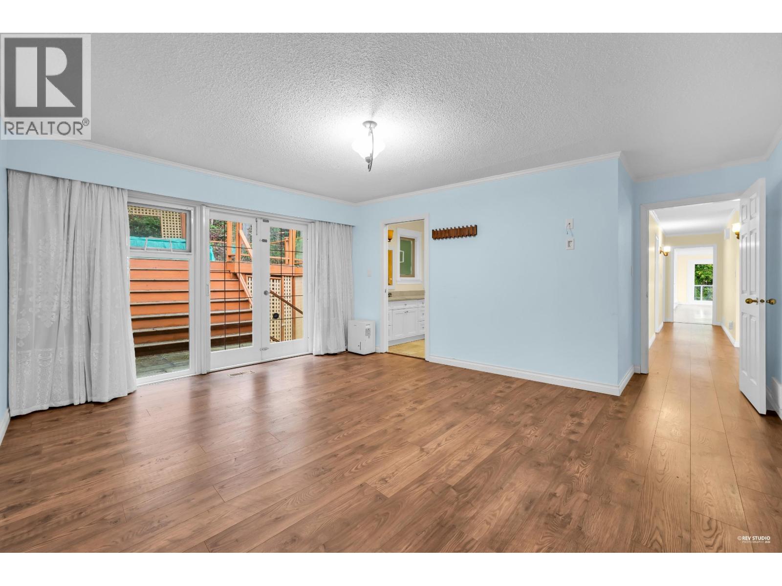 A spacious room with wooden floors and a large window with a view of a pool and deck.