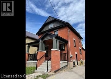 A red brick house with a black roof and a porch with a black railing.