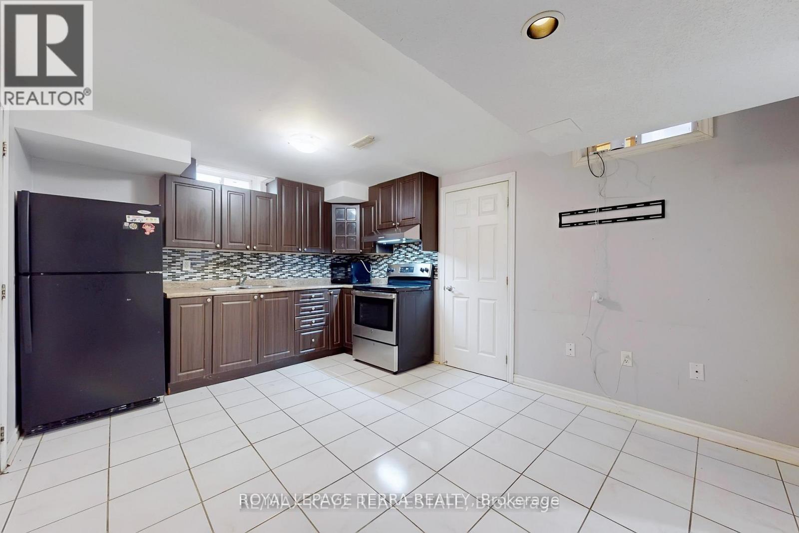 A kitchen with a black fridge and a white tiled floor.