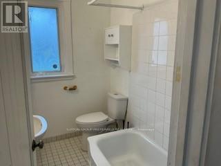 A white bathroom with a toilet, tub, and window.