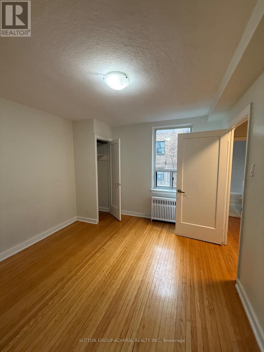 A room with wooden floors and white walls, with a door leading to another room.