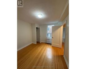A room with wooden floors and white walls, with a door leading to another room.