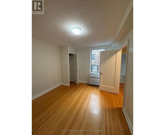 A room with wooden floors and white walls, with a door leading to another room.