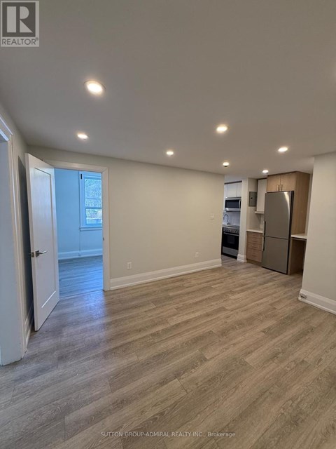 A spacious room with light wood flooring and a kitchenette in the corner.