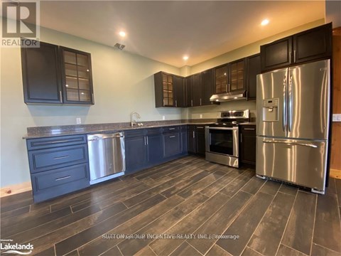 A modern kitchen with dark wood floors and stainless steel appliances.
