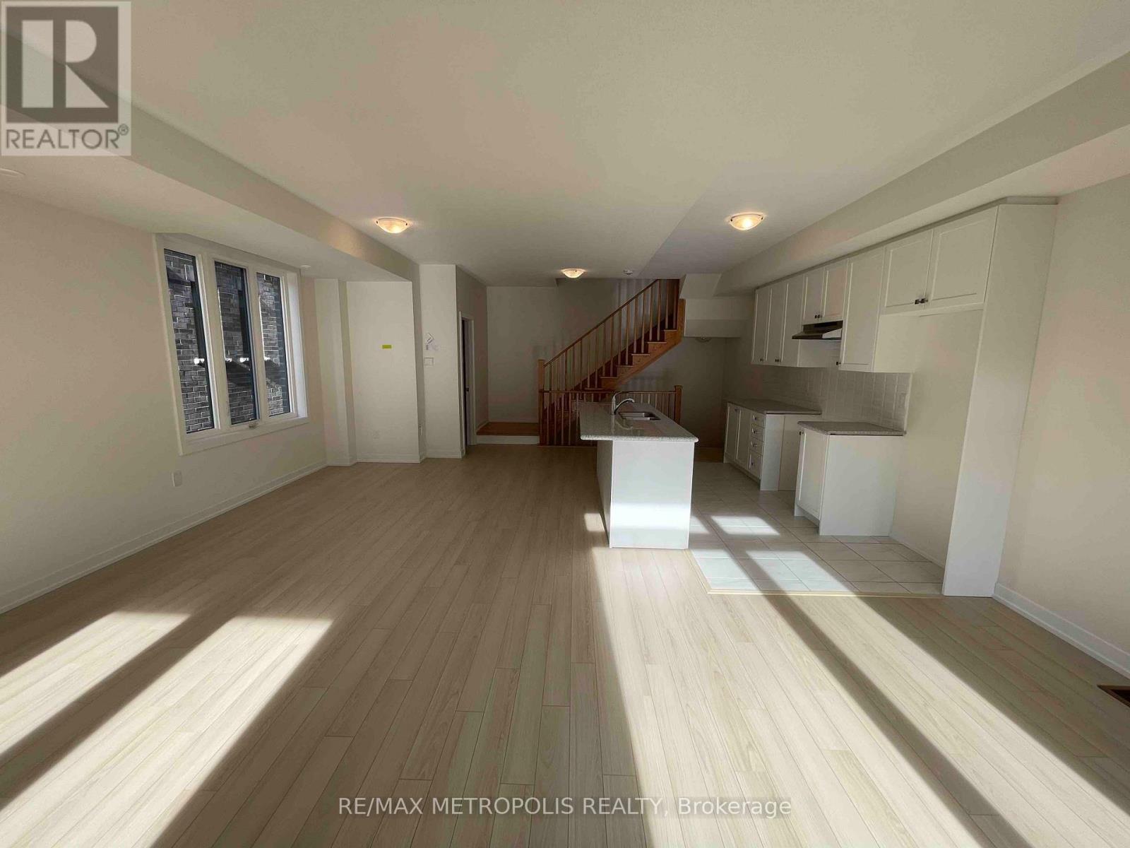 A spacious room with wooden flooring and a staircase leading to the upper level.